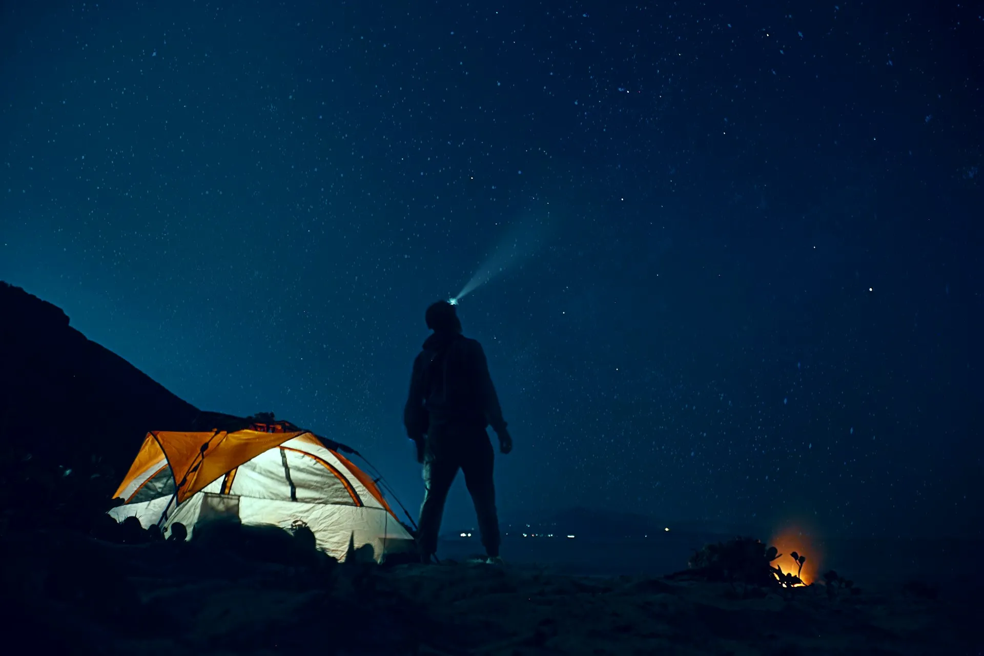 Camper with a headlamp beside a tent at night
